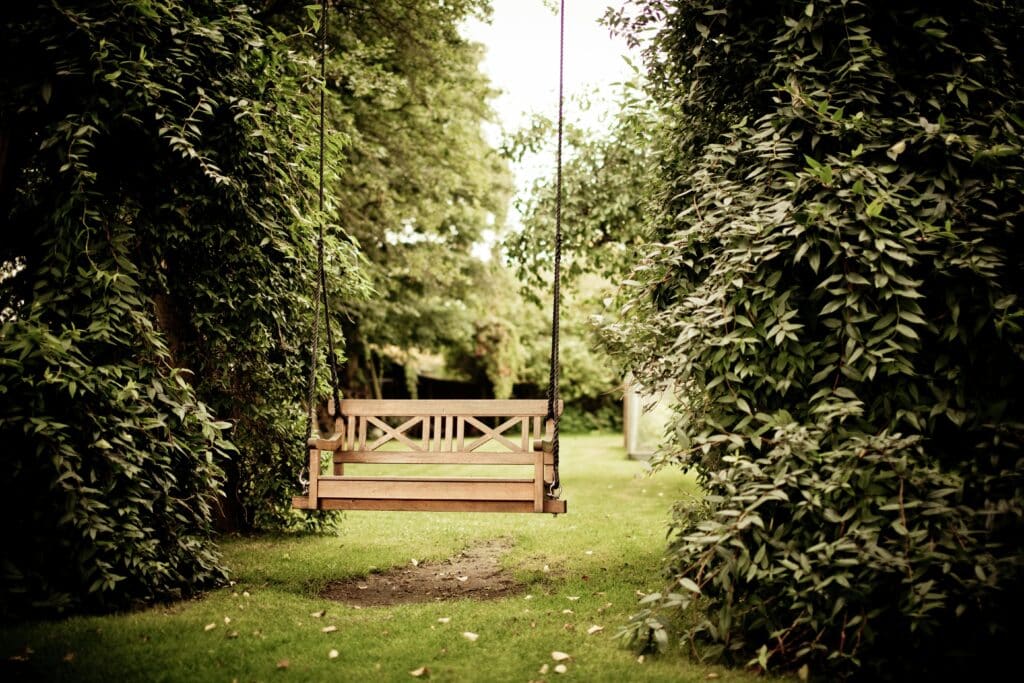 Balancelle en bois suspendue entre des arbres luxuriants dans un jardin verdoyant. Ambiance paisible et romantique.
