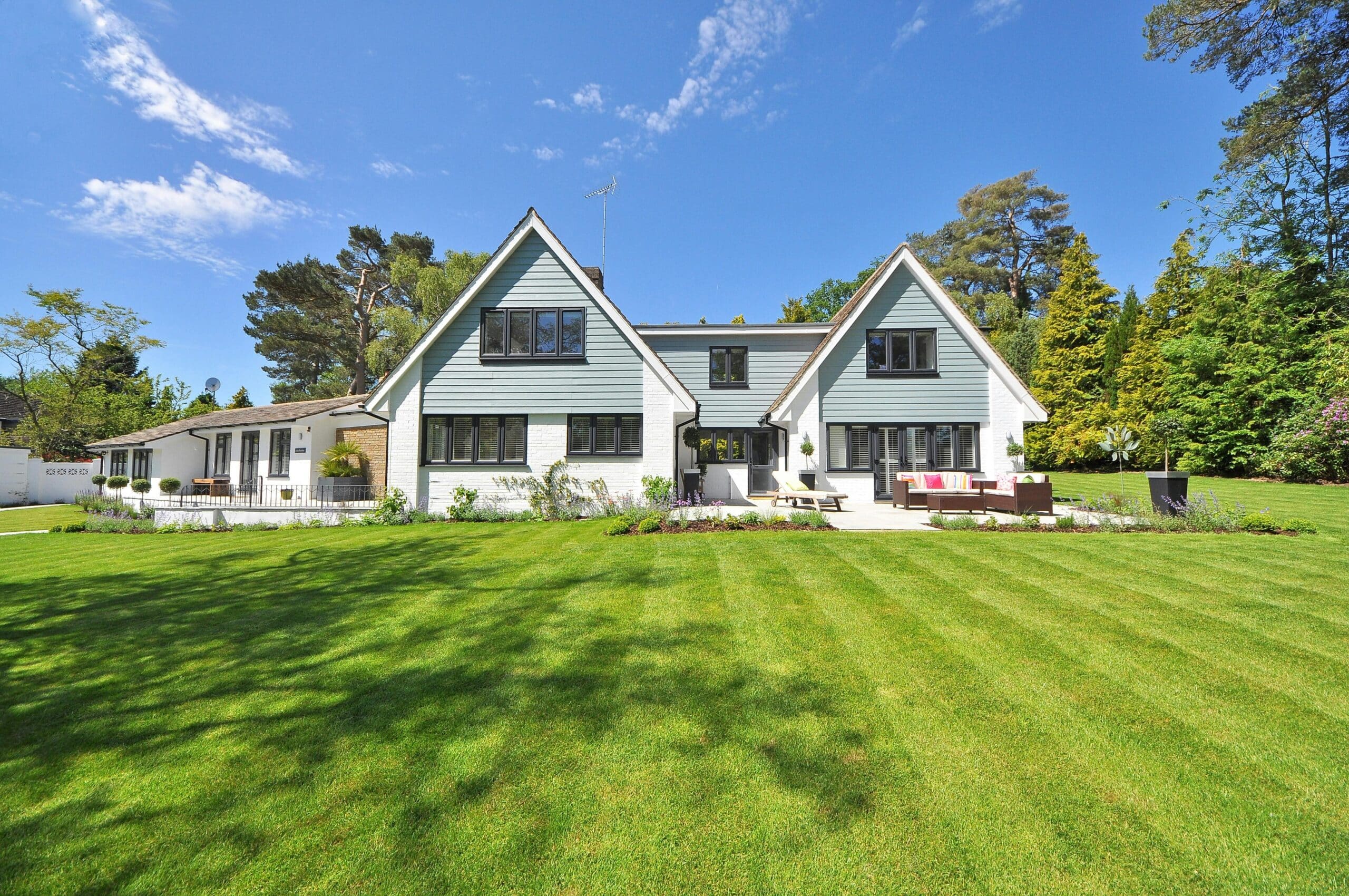 Vue d'une maison de luxe avec pelouse verte bien entretenue sous un ciel bleu. Architecture moderne avec bardage et fenêtres noires.