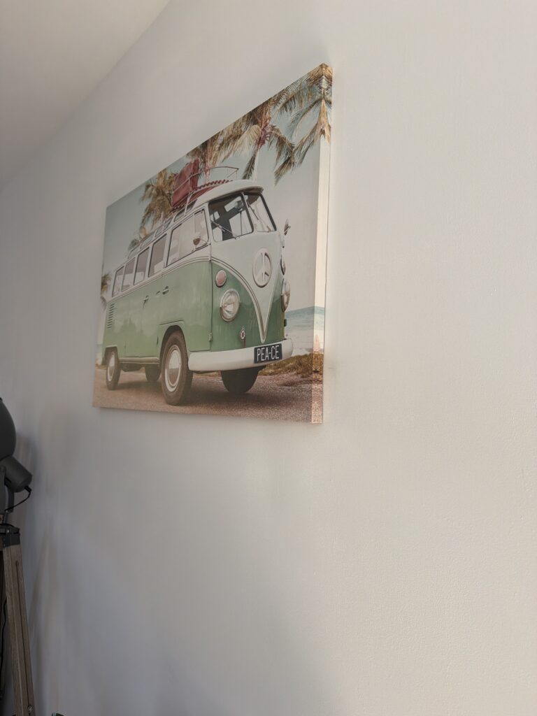 VW Combi vert et blanc avec inscription "PEACE" sur fond de palmiers et plage, accroché sur mur clair.