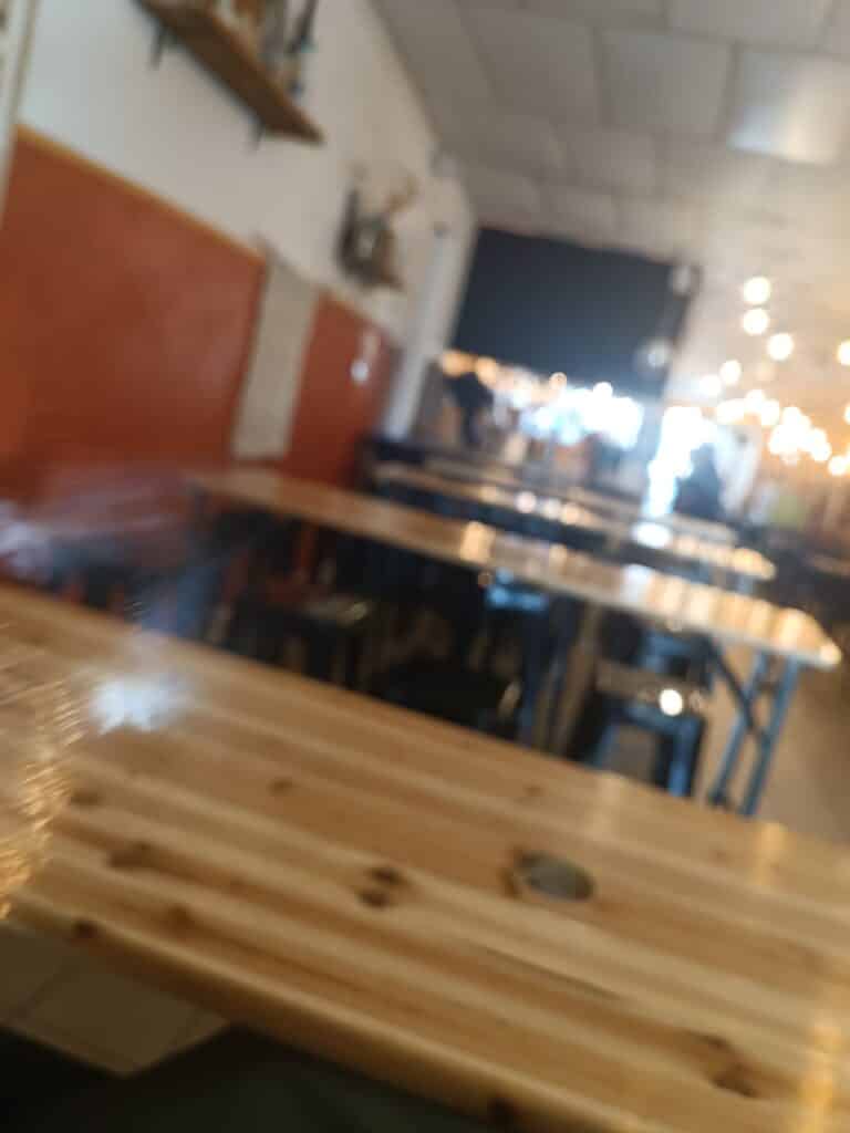 Intérieur de café flou avec grandes tables en bois clair, tabourets noirs et mur orange chaleureux.
