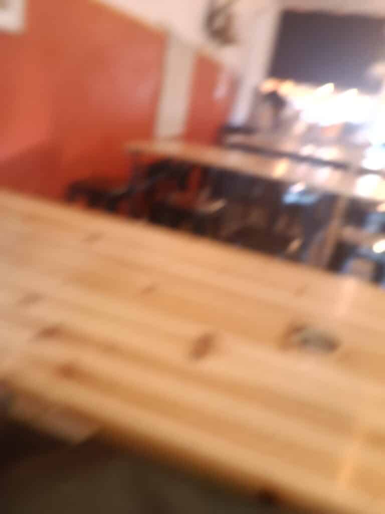 Intérieur flou d'un restaurant avec grandes tables en bois clair devant un mur orange chaleureux.