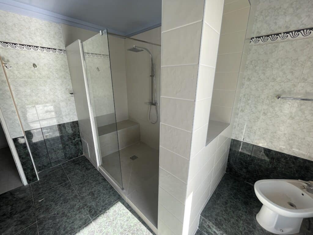 Salle de bain avec douche à l'italienne vitrée, banc intégré et bidet sur carrelage en marbre vert foncé.